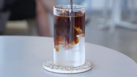 Cinematic-cafe-restaurant-advertisement-concept,-daily-caffeine-fix,-a-glass-of-iced-long-black-with-ice-cubes,-adding-cold-water-and-house-blend-coffee-espresso-and-well-stir-with-a-glass-straw