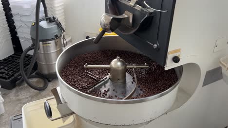 Freshly-roasted-coffee-beans-rotating-and-spinning,-cooling-down-on-the-tray,-food-and-beverage-commodity-concept-shot-at-warehouse-production-factory