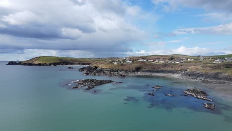 An-aerial-footage-flying-backwards-over-green-blue-waters-of-calm-sunny-Atlantic,-rugged-coastal-line-and-dramatic-sky-in-Ireland