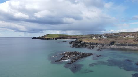 Wide-aerial-footage-flying-backwards-over-green-blue-waters-of-calm-sunny-Atlantic,-rugged-coastal-line-and-dramatic-sky-in-Ireland