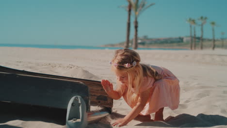 A-little-girl-with-blond-hair-and-flowers-in-her-hair-playing-with-hands-on-sand-on-the-beach-on-a-sunny-day