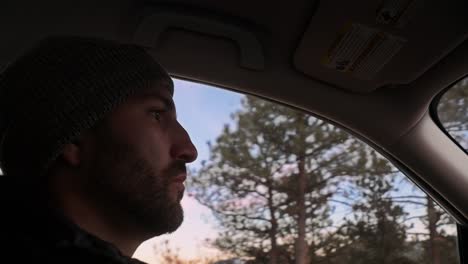 Interior-care-shot-of-a-young-millennial-male-in-a-beanie-driving-through-a-sunset-mountain-landscape
