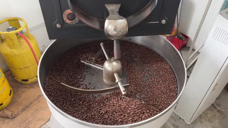 Specialty-coffee-beans-spinning-on-cooling-and-mixing-tray-in-regular-speed-to-reduce-the-heat-evenly-after-roasting,-production-warehouse-factory-shot-of-food-and-beverage-industry,-tilt-down-shot