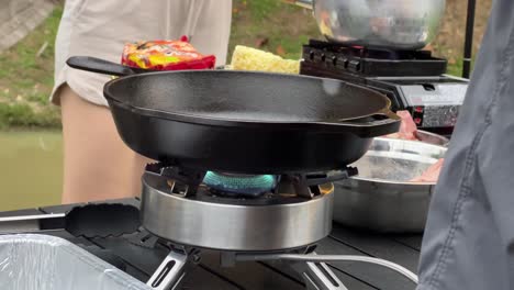 Heating-up-the-cast-iron-pan,-chef-placing-his-hand-above-the-pan,-making-sure-it-is-hot-and-ready-to-cook-the-steaks,-outdoor-glamping-environment