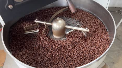 Specialty-coffee-beans-spinning-on-cooling-and-mixing-tray-to-reduce-the-heat-evenly-after-roasting,-production-warehouse-factory-shot-of-food-and-beverage-industry,-tilt-down-shot