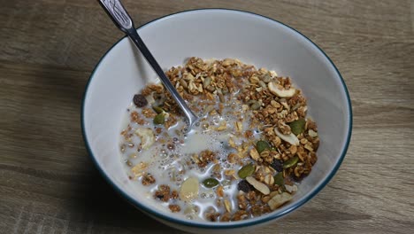 A-zoom-in-of-the-a-bowl-of-Granola-and-Almond-Milk-just-poured-in-making-bubbles,-seeds,-dried-fruits,-healthy-breakfast