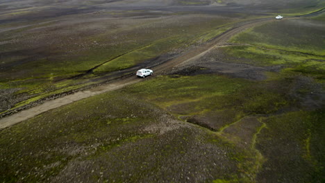 White-4x4-car-driving-through-Icelandic-highlands,-black-volcanic,-rock-landscape,-on-off-road-dirt-track-road