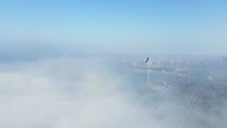 FOG-IN-UAE:-Aerial-view-of-Fog-over-Sharjah's-Khalid-Lake,-Sharjah-skyline-and-flag-island-covered-in-the-winter-morning-fog,-United-Arab-Emirates,-4K-Drone-Footage