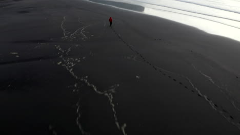 Drone-footage-of-man-on-stokkness-beach-panning-up-towards-dramatic-mountains-on-the-coast-of-southern-Iceland