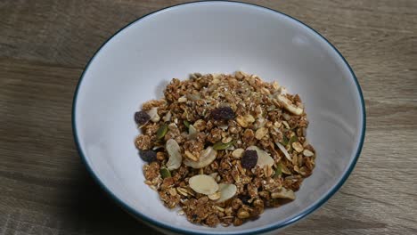 Zoom-in-of-a-Bowl-with-Granola-on-the-table,-nuts,-raisins,-seeds,-dried-fruits,-healthy-breakfast