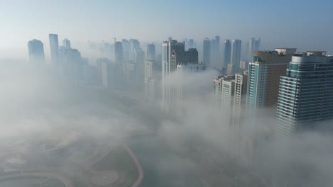 FOG-IN-UAE:-Aerial-view-of-Fog-over-Sharjah's-Khalid-Lake,-Sharjah-skyline-covered-in-the-winter-morning-fog,-United-Arab-Emirates,-4K-Drone-Footage