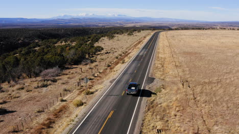 Drone-shot-following-a-blue-car-running-on-a-countryside-highway-in-Norwood,-Colorado