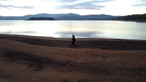 Silhouette-Einer-Person,-Die-Am-Goldenen-Sandstrand-Des-Lake-Jindabyne,-New-South-Wales,-Australien,-Spazieren-Geht