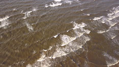 Aerial-shot-of-waves-crashing-onto-the-beach,-dark-murky-sea-water
