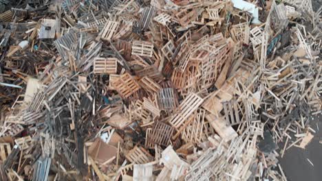 Aerial-top-down-view-tilting-downwards-closely-across-huge-dumpsite-filled-with-tons-of-wooden-and-bulky-waste-amde-up-of-euro-pallets