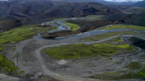 Revelando-Imágenes-De-Drones-De-Una-Pista-Todoterreno-Que-Conduce-A-Un-Sistema-Fluvial-En-Un-Valle-Con-Montañas-Como-Telón-De-Fondo-En-Las-Tierras-Altas-De-Islandia