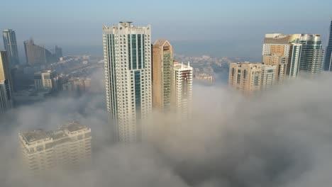 FOG-IN-UAE:-Top-view-of-dense-Fog-over-Sharjah's-Al-Majaz-area,-Sharjah-skyline-covered-in-the-winter-morning-fog,-United-Arab-Emirates,-4K-Drone-Footage