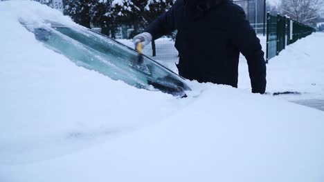 The-young-man-is-cleaning-the-car's-front-window-from-the-snow-with-a-yellow-brush-in-winter