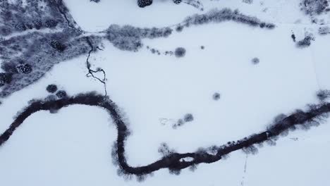 Aerial-view-over-a-mountain-river-covered-in-snow-in-winter