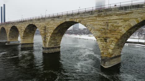 Drohne-Fliegt-Im-Winter-Zwischen-Der-Berühmten-Steinbogenbrücke-In-Der-Innenstadt-Von-Minneapolis
