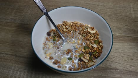 Granola-in-a-bowl-with-a-spoon-and-Almond-Milk-just-poured-in-making-bubbles,-seeds,-dried-fruits,-healthy-breakfast