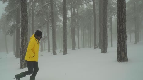 A-man-walks-alone-through-a-white-and-snowy-forest-while-wearing-a-bright-yellow-jacket