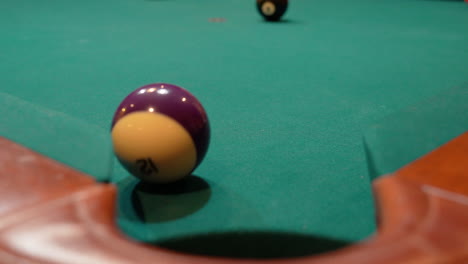 Pool-Balls-are-Broken-on-an-8-Ball-Triangle-Rack-and-the-Purple-Stripe-12-Ball-Slowly-Rolls-towards-Edge-of-Corner-Pocket,-Closeup-with-Solids-and-Stripes-Scattering-Across-the-Table-with-Green-Felt