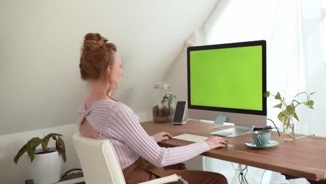 Young-beautiful-woman-sitting-in-front-of-a-monitor-with-green-screen-chroma-key