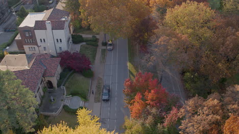 Overhead-view-of-Wydown-Boulevard-as-cars-drive-down-the-street-and-the-camera-pulls-back-over-beautiful-Autumn-trees