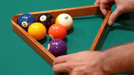 Person-Racks-9-Ball-Pool-Diamond-Closeup-on-the-Spot-then-Rearranges-Solid-and-Striped-Billiard-Balls-on-Table-with-Green-Felt-or-Cloth-and-Tightening-Rack-with-Hands-before-Lifting-Wooden-Triangle