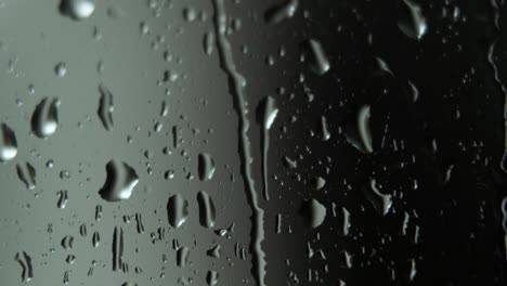 Rain-water-droplets-falling-down-on-window-glass,-reflecting-liquid-shapes,-macro-shot
