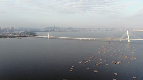 Hong-Kong-Shenzhen-Bay-Bridge-Mit-Tin-Shui-Wai-Gebäuden-Am-Horizont-Und-Fisch--Und-Austernzuchtbecken,-Luftbild