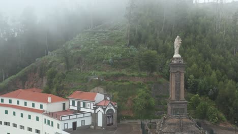 Spiritual-shrine-on-lush-mountains-with-mist-above-city-of-Funchal,-aerial