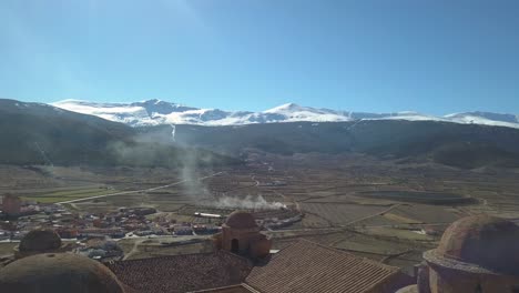 Aerial-descending-shot-with-over-the-castle-of-La-Calahorra-with-the-mountain-of-Sierra-Nevada-behind