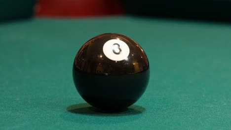 Black-Eight-Ball-Zeigt-Die-Reflexion-Eines-Mannes,-Der-Ihn-Anspricht-Und-In-Die-Ecktasche-Eines-Brunswick-Billardtisches-Schießt,-Nachdem-Er-Übungsschläge-Mit-Einem-Cue-Ball-Gemacht-Hat,-Nahaufnahme-Mit-Grünem-Filz-Oder-Stoff