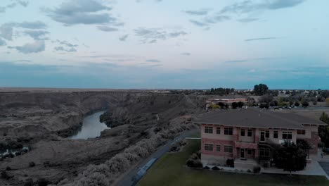 Slow-aerial-pan-and-rising-shot-over-a-small-building-next-to-the-Snake-River-Canyon-in-Twin-Falls,-Idaho-at-dusk