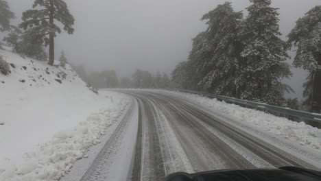 View-out-the-front-of-a-car-driving-down-a-snowy-mountain-road