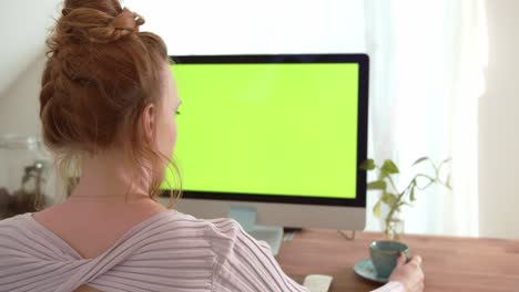 Young-women-sitting-in-front-of-computer-with-green-screen-mock-up