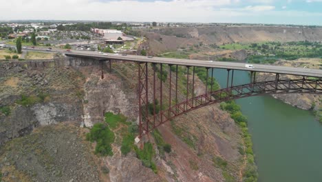 Slow-motion-upward-aerial-tilt-of-vehicles-driving-across-the-Snake-River-Canyon-in-Twin-Falls,-Idaho-with-half-of-the-Perrine-Memorial-Bridge-in-Frame