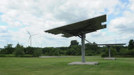 Large-solar-panels-adjust-position-as-sun-light-changes-with-wind-turbines-in-background