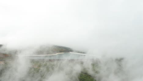 Fog-creates-low-visibility-around-man-made-water-reservoir-in-mountains,-aerial