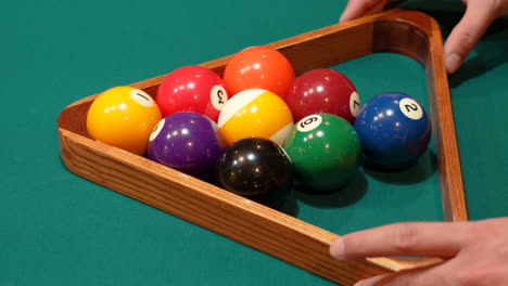 Man-Rolls-9-Ball-Pool-Diamond-Rack-into-Frame-on-the-Spot-Closeup-on-a-Table-with-Green-Felt-or-Cloth-and-Tightens-Rack-with-Hands-before-Lifting-Wooden-Triangle