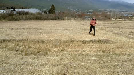 Young-woman-chasing-after-dog-running-through-remote-field-in-Chinese-mountains