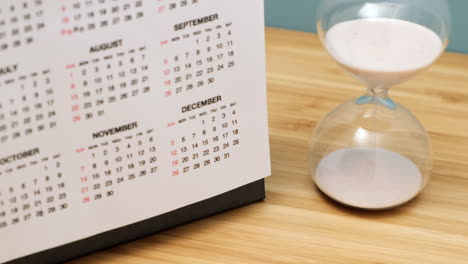 Close-up-of-a-calendar-and-hourglass-on-wooden-table