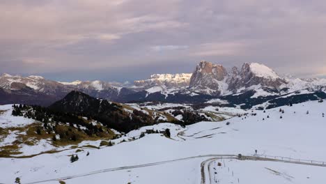 Aerial-shot-of-road-in-snow-leading-to-panoramic-view-of-mountain-range-at-alpine-meadow-Seiser-Alm---Alpe-di-Siusi-in-the-Dolomites,-Italy
