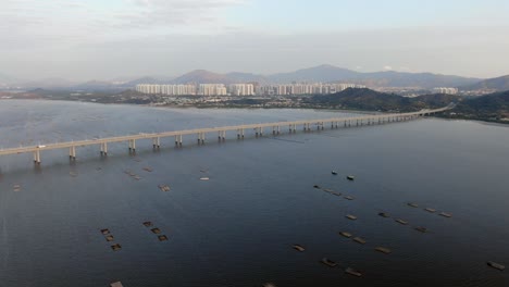 Hong-Kong-Shenzhen-Bay-Bridge-with-Tin-Shui-Wai-buildings-in-the-horizon-and-Fish-and-Oyster-cultivation-pools,-Aerial-view
