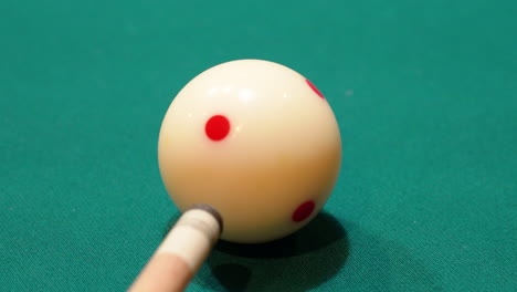 Billiards-Closeup-of-White-Cue-Ball-with-Red-Spots-being-Quickly-Shot-on-a-Pool-Table-by-Wooden-Cue-Stick-Tip-Hovering-Above-Green-Felt-after-Several-Practice-Strokes,-No-Faces