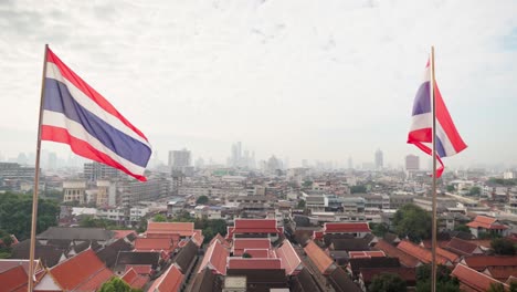 4k-Dos-Banderas-Del-Estado-Tailandés-Ondeando-En-El-Viento-Con-Bangkok-Al-Fondo