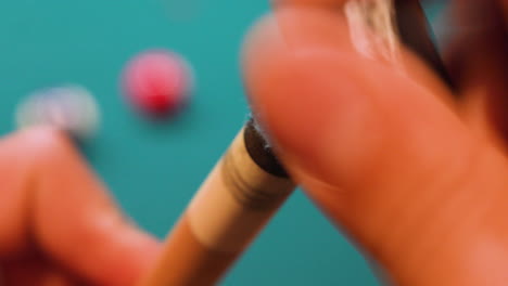 Person-Chalking-Tip-of-Pool-or-Snooker-Cue-with-Blue-Chalk-on-Wooden-Stick-Closeup-using-grinding-and-brushing-motion-with-Pool-Balls-and-Blue-Felt-in-background,-No-Faces,-Billiards
