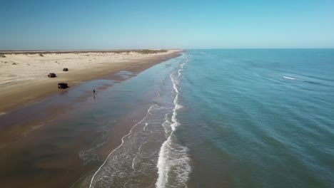 Aerial-drone-view-following-the-shoreline-and-beach-at-low-tide-on-a-gulf-coast-barrier-island-on-a-sunny-afternoon---South-Padre-Island,-Texas